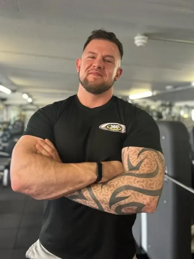 A personal trainer standing on the gym floor with his arms folded